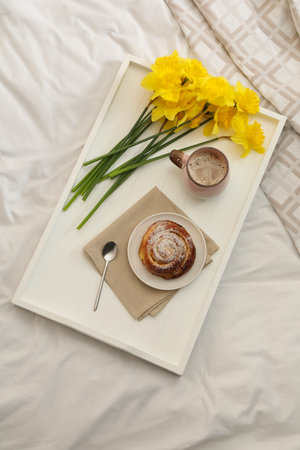 Bouquet of beautiful daffodils, bun and coffee on bed, top viewの写真素材