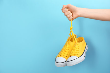 Woman holding pair of sneakers on light blue background, closeup. Space for textの写真素材