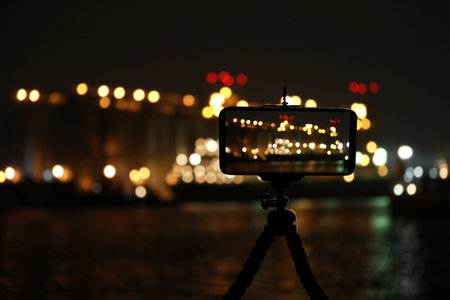 Taking photo of beautiful cityscape at night with smartphone mounted on tripodの写真素材
