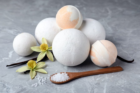 Fragrant bath bombs, sea salt, vanilla sticks and flowers on gray marble tableの写真素材