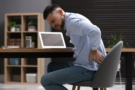 Man suffering from back pain while working with laptop in office. Symptom of poor postureの写真素材