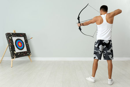 Man with bow and arrow aiming at archery target indoors