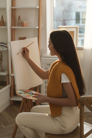 Beautiful young woman drawing on easel at homeの写真素材