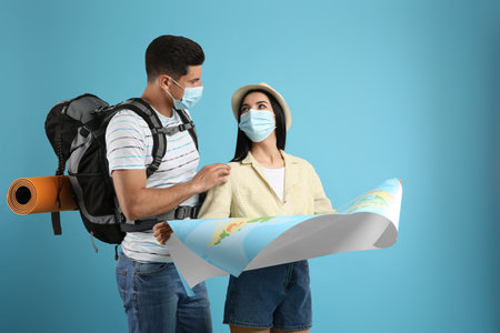 Couple of tourists in medical masks with map on light blue background.