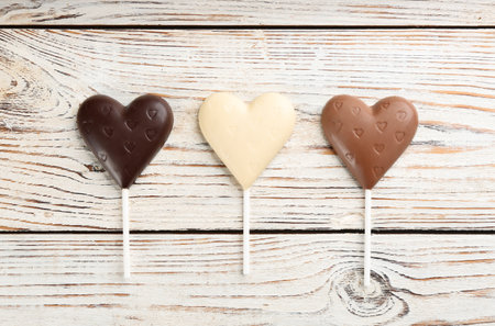 Different chocolate heart shaped lollipops on white wooden table, flat layの写真素材