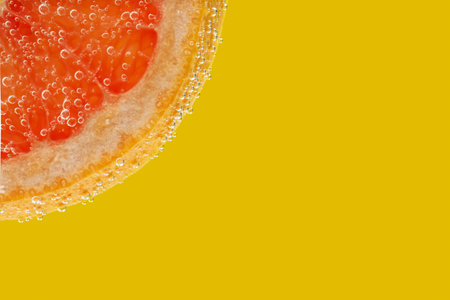 Slice of grapefruit in sparkling water on yellow background, closeup with space for text. Citrus sodaの写真素材