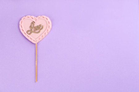 Chocolate heart shaped lollipop with word Love on light lilac background, top view. Space for textの写真素材
