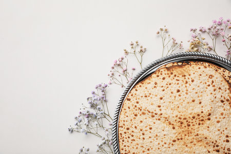 Tasty matzos and fresh gypsophila flowers on light gray background, flat lay with space for text....