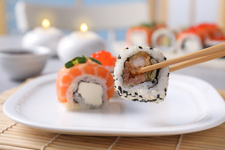 Taking tasty sushi roll from plate with chopsticks on table, closeupの写真素材