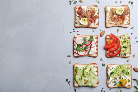 Different delicious sandwiches with microgreens on gray table, flat lay. Space for textの写真素材