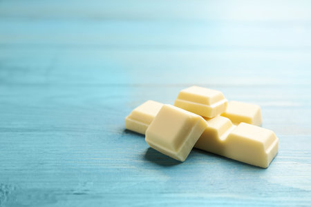 Pieces of tasty sweet chocolate on light blue wooden table, closeup. Space for textの写真素材