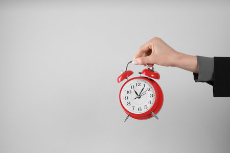 Businesswoman holding alarm clock on light gray background, closeup with space for text. time managementの写真素材