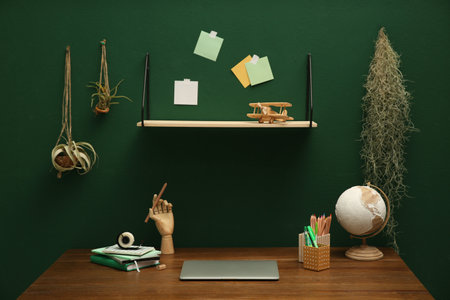 Stylish workplace with laptop on wooden desk and different decor near green wall. interior designの写真素材