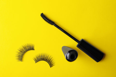 Black mascara and fake eyelashes on yellow background, flat lay. makeup productの写真素材