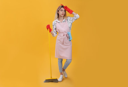 Young housewife with broom on yellow backgroundの写真素材