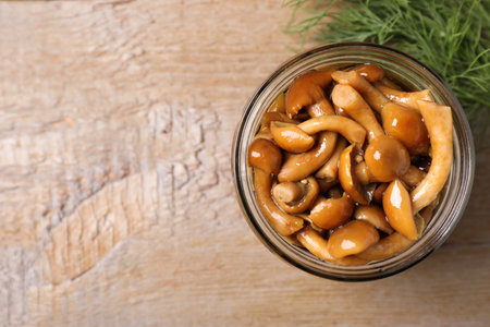 Delicious marinated mushrooms in glass jar and dill on wooden table, flat lay. Space for textの写真素材