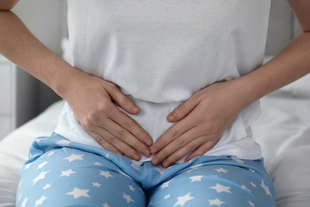 Woman suffering from abdominal pain on bed at home, closeupの写真素材