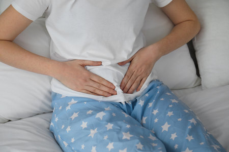 Woman suffering from abdominal pain on bed at home, closeupの写真素材