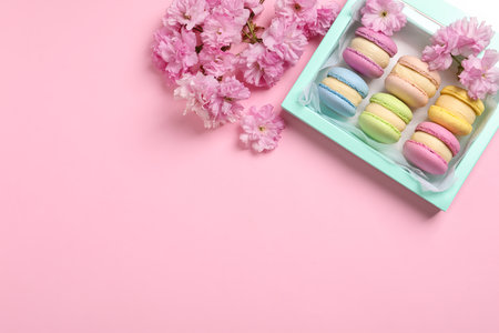 Many delicious colorful macarons in box and flowers on pink background, flat lay. Space for textの写真素材