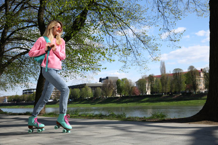 Beautiful young woman roller skating outdoors on sunny day