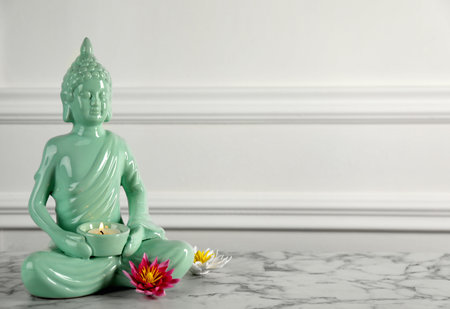 Buddha statue with burning candle and lotus flowers on white marble table. Space for textの写真素材