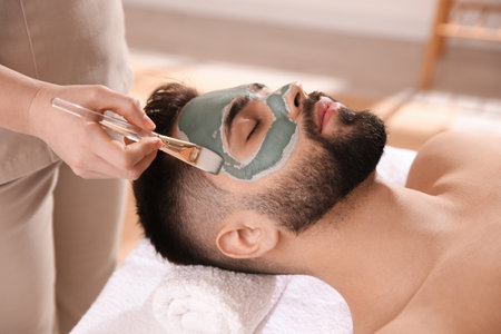 Cosmetologist applying mask on man's face in spa salonの写真素材