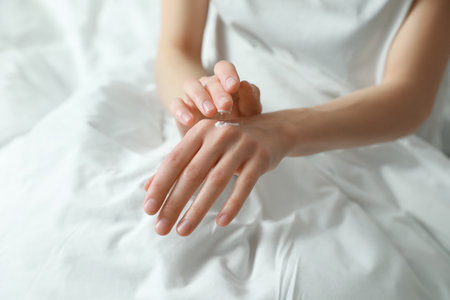 Woman applying hand cream in bed, closeupの写真素材
