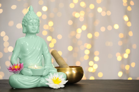 Buddha statue with candle, lotus flowers and singing bowl on table against blurred lights. Space for textの写真素材