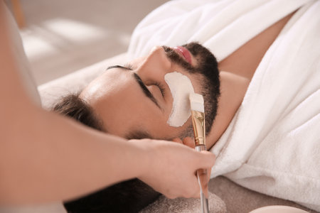 Cosmetologist applying mask on man's face in spa salonの写真素材