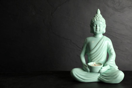 Buddha statue with burning candle on black table. Space for textの写真素材