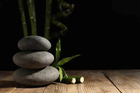 Spa stones and bamboo stems on wooden table against dark background, space for textの写真素材