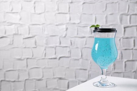 Light blue drink in glass with lid on white table, space for text