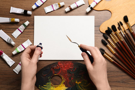 Man with paint, spatula and blank canvas on wooden table, top viewの写真素材