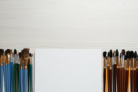 Blank canvas and brushes on white wooden table, flat lay. Space for textの写真素材
