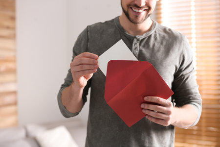 Man holding envelope with blank greeting card indoors. close-up