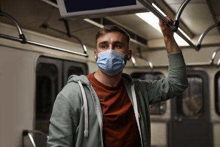 Young man in protective mask with earphones traveling by subway train. public transportの写真素材