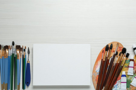 Blank canvas, tools, palette and paints on white wooden table, flat lay. Space for textの写真素材
