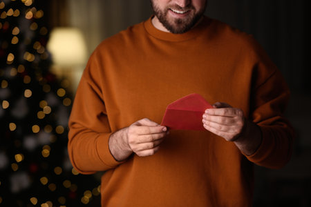 Man holding envelope with greeting card against blurred Christmas lights, closeupの写真素材