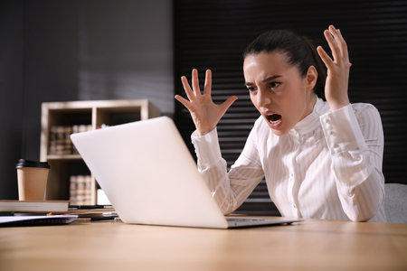 Emotional young businesswoman working on laptop in office. online hate conceptの写真素材