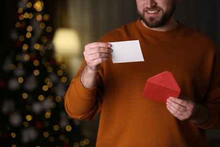 Man holding envelope and greeting card against blurred Christmas lights, closeupの写真素材