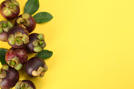 Fresh ripe mangosteen fruits with green leaves on yellow background, flat lay. Space for textの写真素材