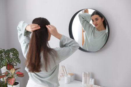 Young woman doing hair near mirror at home. morning routineの写真素材