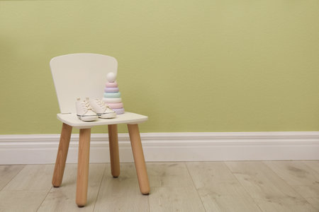 Chair with baby shoes and toy near green wall, space for text. interior designの写真素材