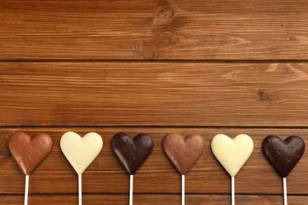 Different chocolate heart shaped lollipops on wooden table, flat lay. Space for textの写真素材