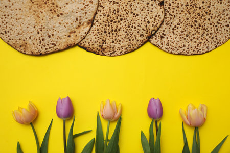 Tasty matzos and fresh flowers on yellow background, flat lay. Passover (Pesach) celebrationの写真素材