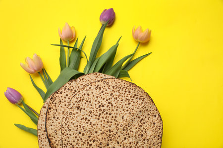 Tasty matzos and fresh flowers on yellow background, flat lay. Passover (Pesach) celebrationの写真素材