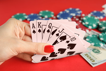Woman holding playing cards with royal flush combination at red table, closeup