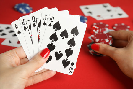 Woman holding playing cards with royal flush combination and poker chips at red table, closeupの写真素材