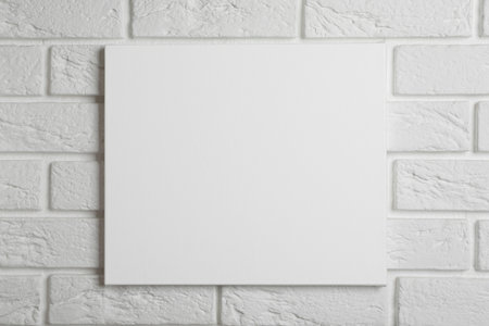 Blank canvas hanging on white brick wall, space for textの写真素材