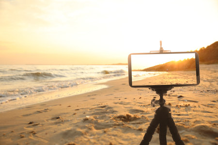 Taking photo of beautiful sandy beach with smartphone mounted on tripodの写真素材